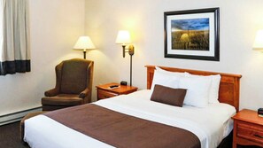 A hotel room with a large bed, a chair, two bedside tables, a lamp, and a framed picture on the wall.