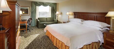 A hotel room with a large bed, a desk with a chair, a sofa, and two lamps.