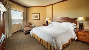 A hotel room with a large bed, two bedside lamps, a chair, a dresser, and a window with curtains.