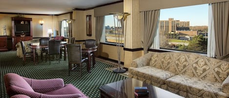 A hotel room with a sofa, armchairs, a dining table, and a TV.