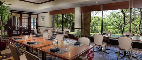 A conference room with a large table, chairs, and large windows offering a view of trees and a pond.