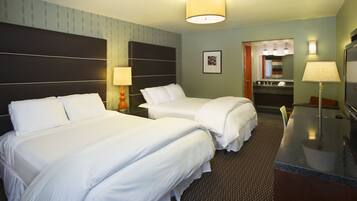 A hotel room with two beds, a desk, a chair, a lamp, a mirror, and a bathroom visible through an open door.