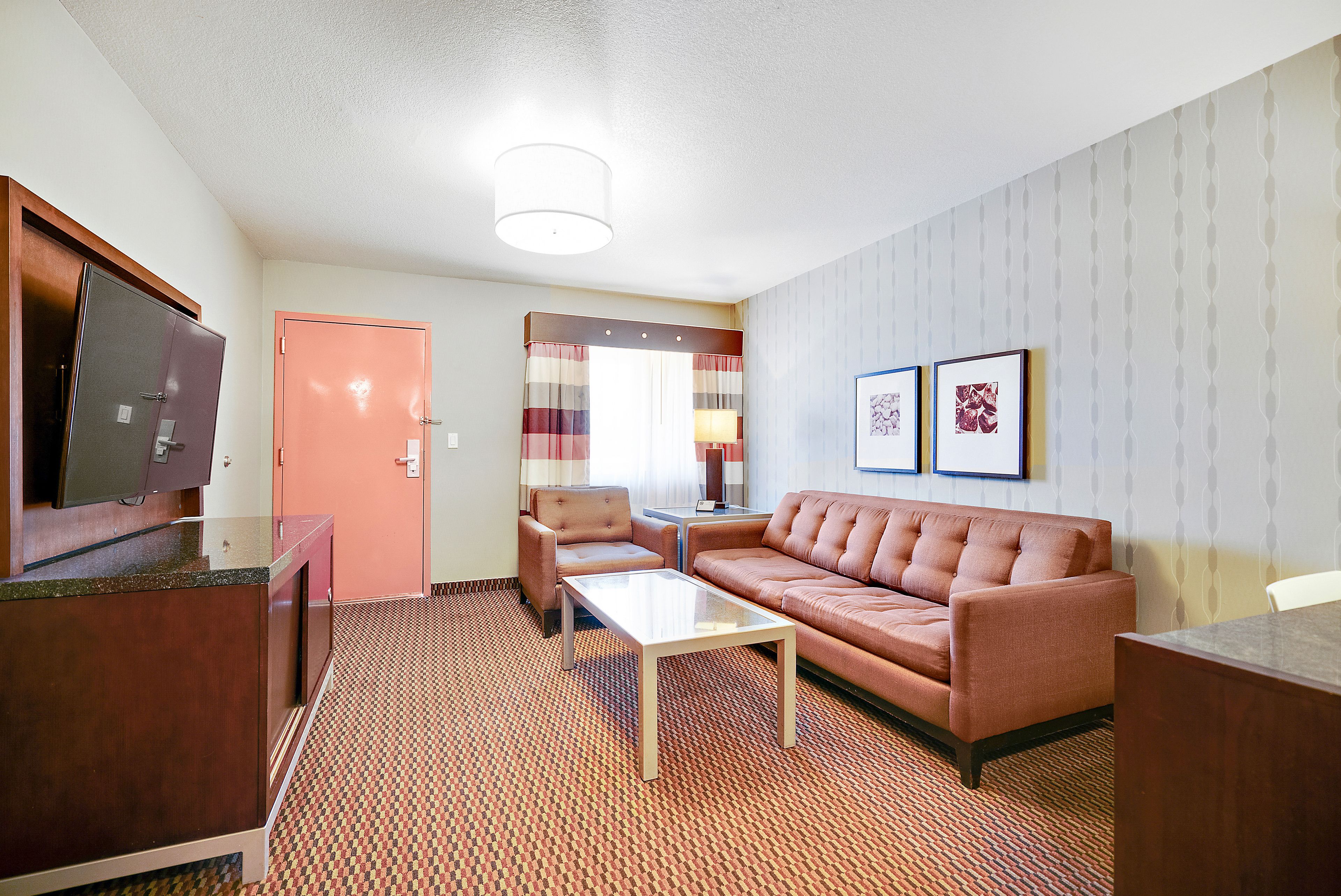 Ett hotellrum med en soffa, ett soffbord, en tv och en dörr.