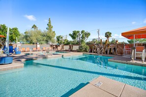 A clear swimming pool with lounge chairs and umbrellas, surrounded by trees and a fence.