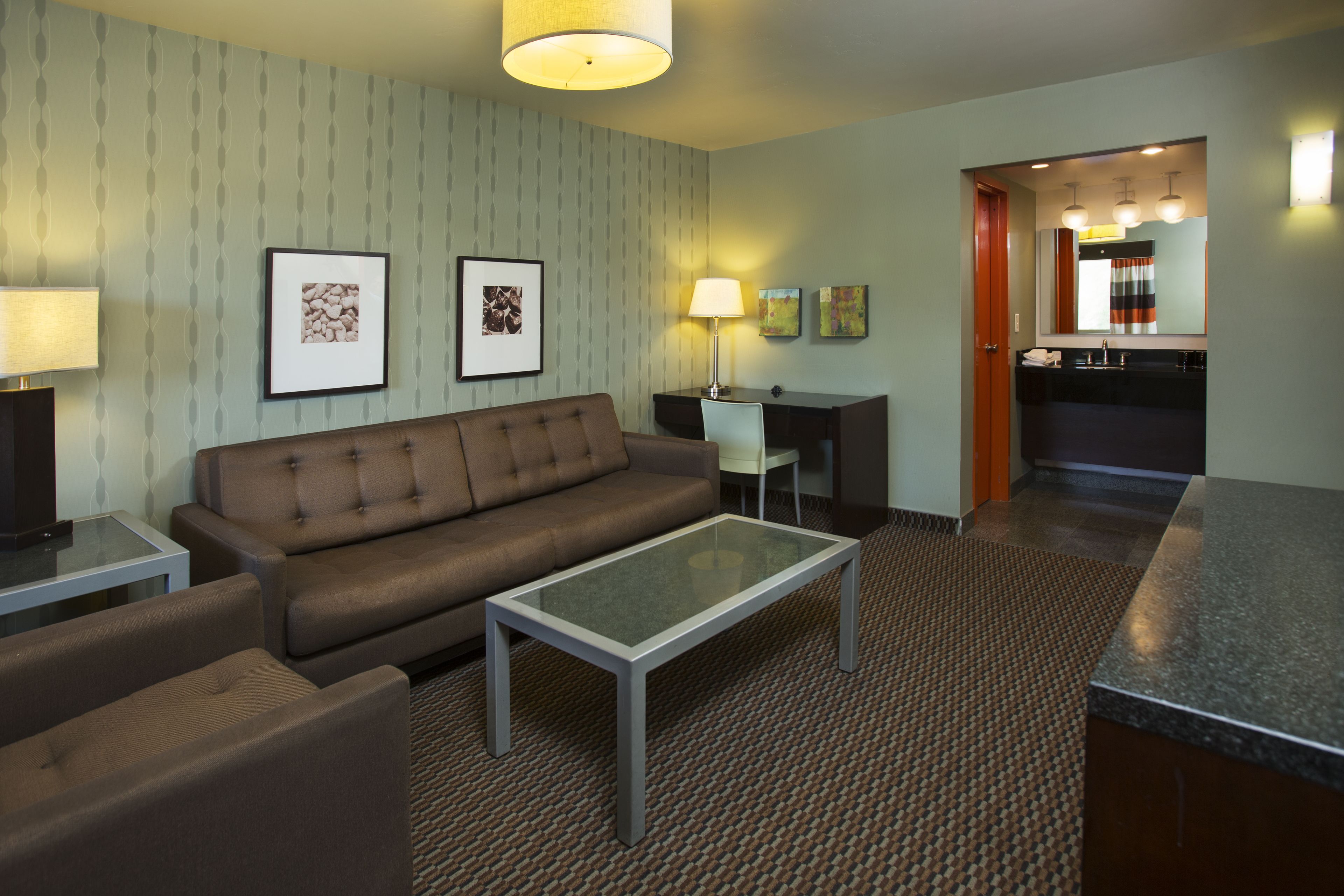A hotel room with a sofa, a glass-top coffee table, a desk, and a kitchenette area.