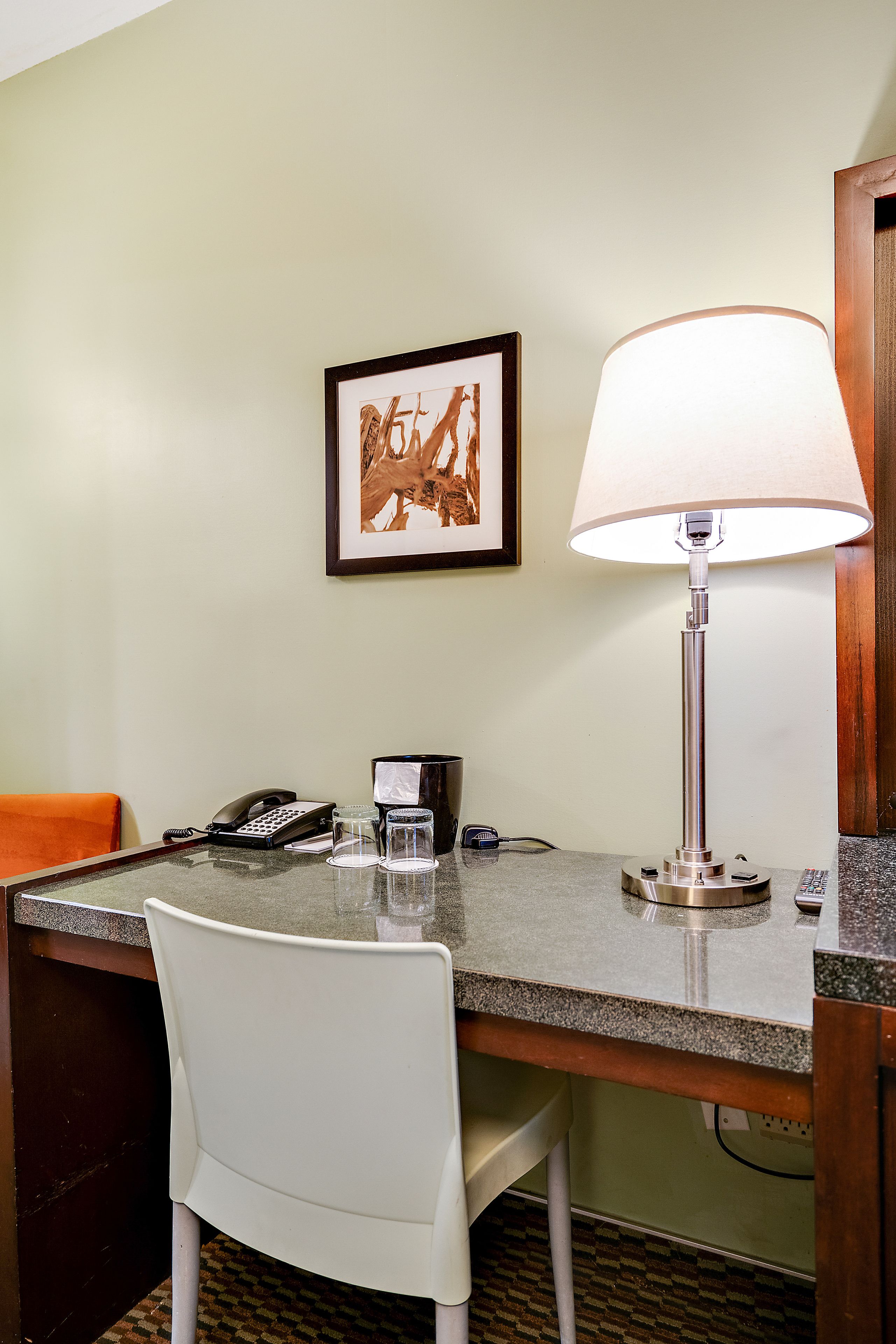 Una habitación de hotel con escritorio, una silla, una lámpara, un cuadro en la pared y un teléfono.