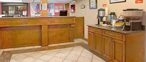 A hotel lobby with a reception desk, a coffee station, and a framed picture on the wall.