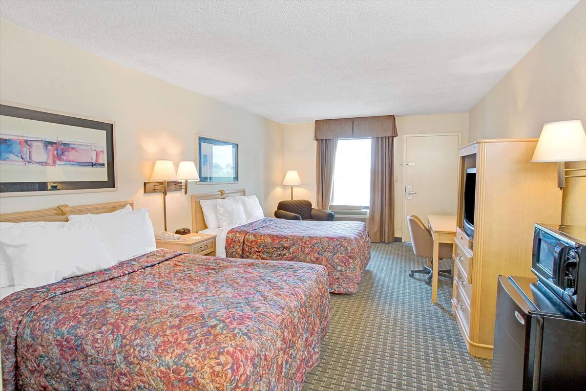 Ein Hotelzimmer mit zwei Betten, einem Schreibtisch, einem Sessel, einem Fernseher und einem Kühlschrank.