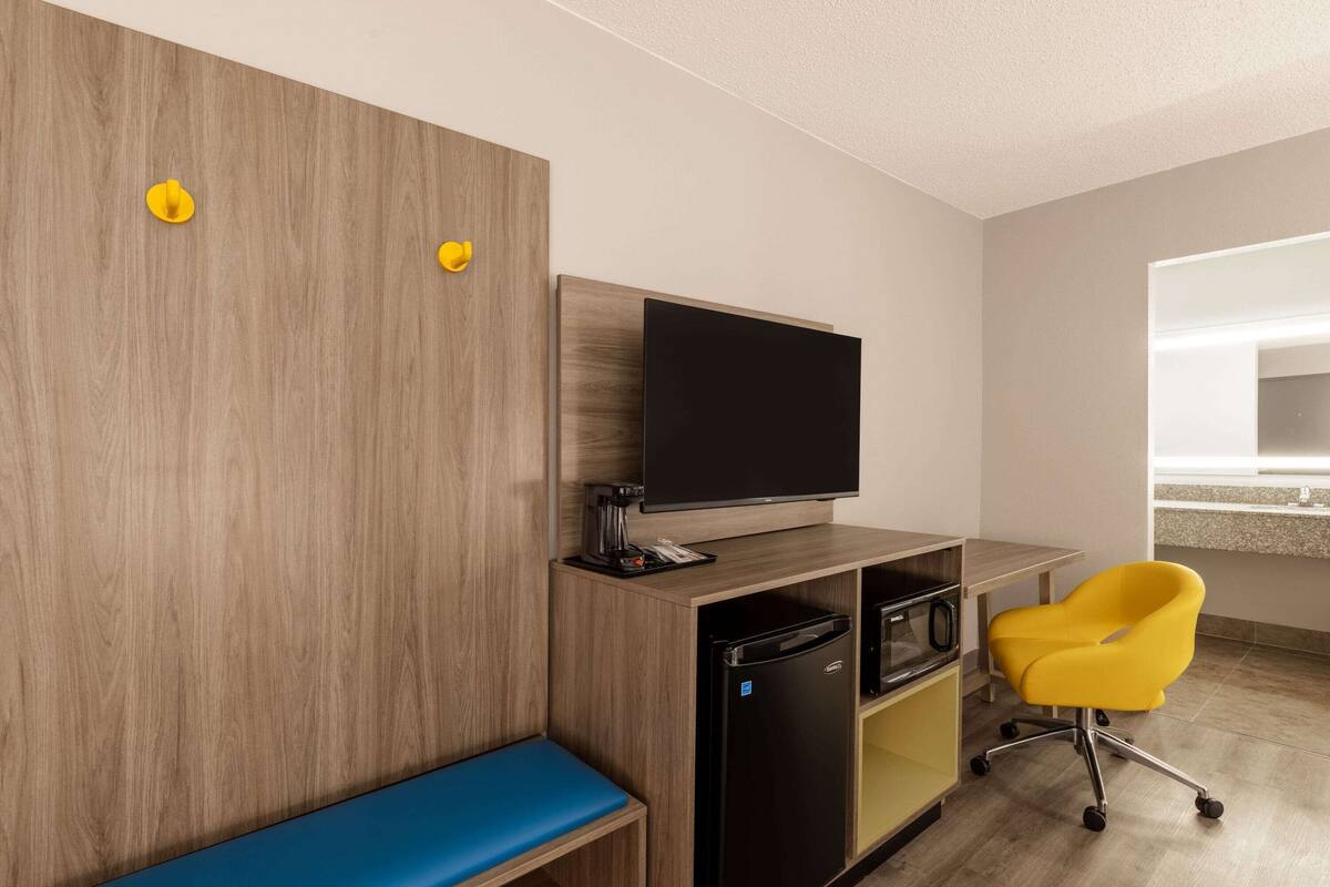Ein modernes Hotelzimmer mit einem Holzschrank, einem Flachbildfernseher, einem gelben Sessel und einer blauen Bank.