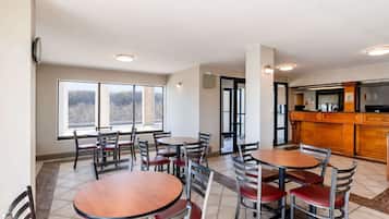 A dining area with multiple tables and chairs, a kitchen area with a bar, and large windows offering a view of the outdoors.