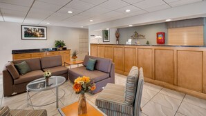 A modern hotel lobby with a brown sofa, a striped armchair, a glass coffee table, and a wooden reception desk.