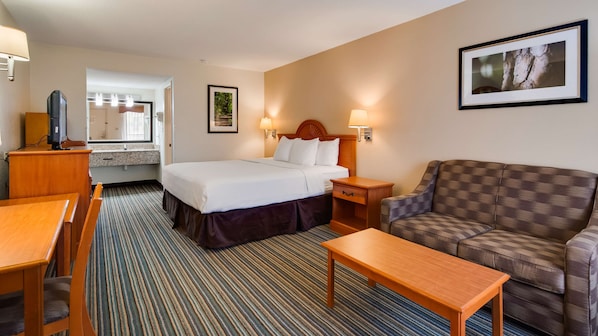A hotel room with a bed, a sofa, a desk, a chair, a TV, and a picture on the wall.