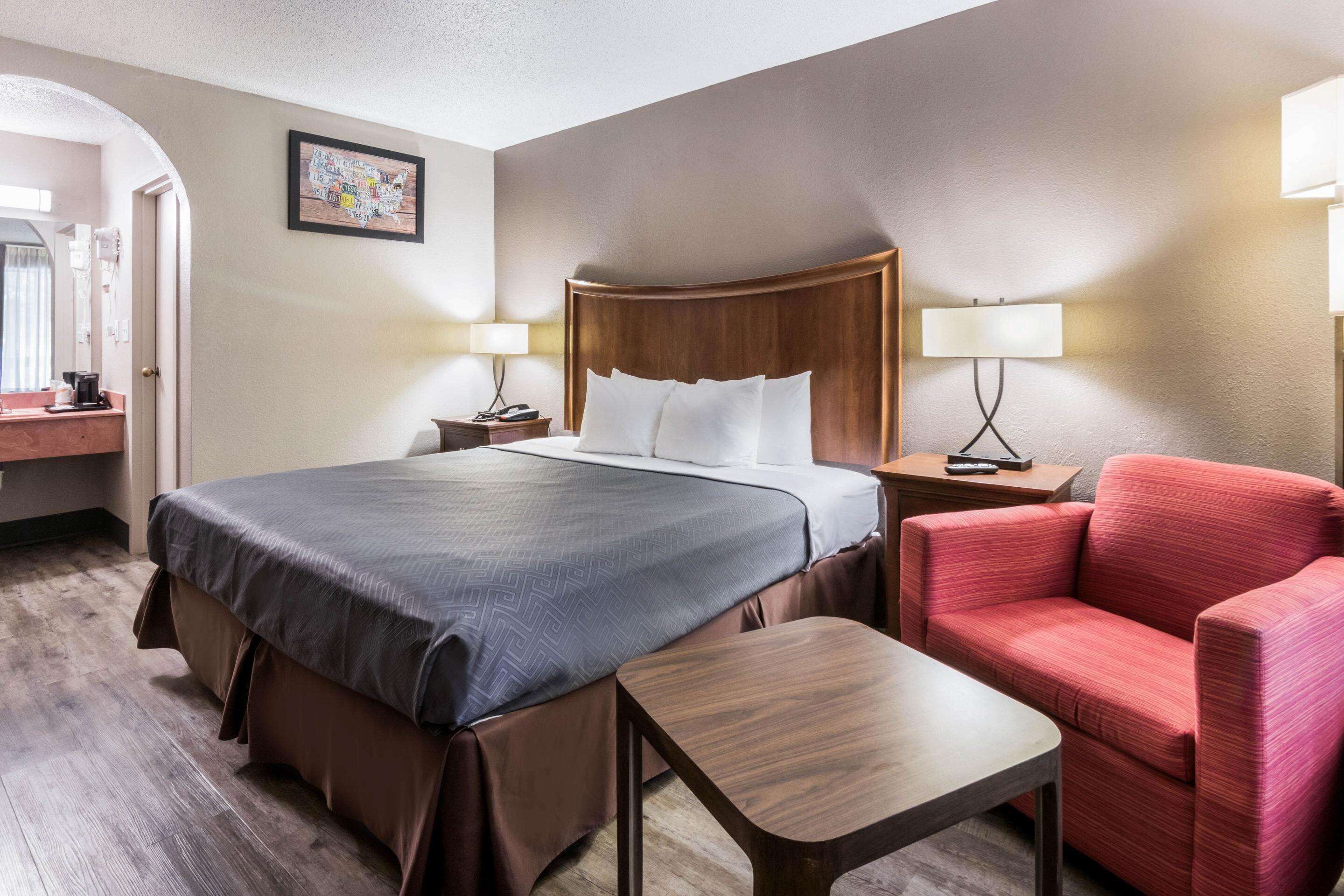 A hotel room with a large bed, two bedside tables, a chair, a small table, and a mirror.