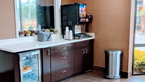 A kitchenette with a refrigerator, a coffee machine, and a trash can.