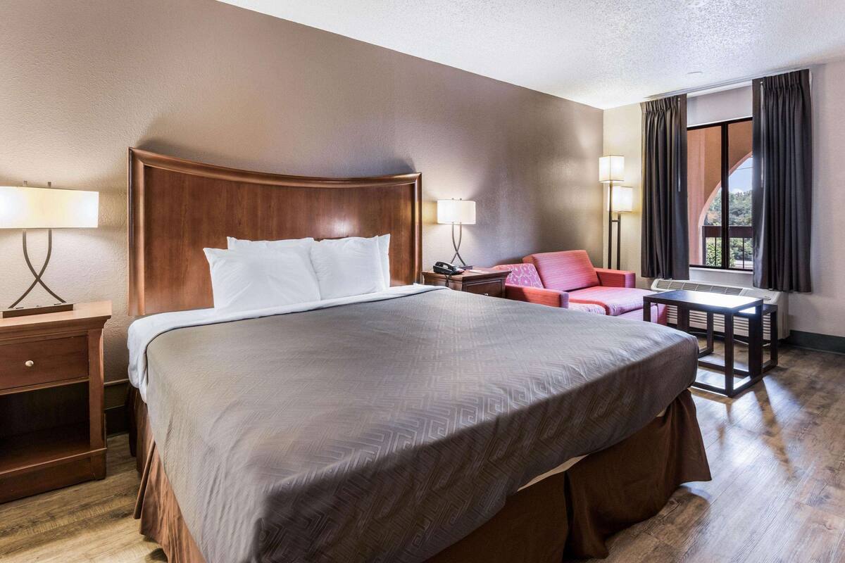 Quarto de hotel com uma cama grande, uma escrivaninha, uma cadeira e uma janela com cortinas.