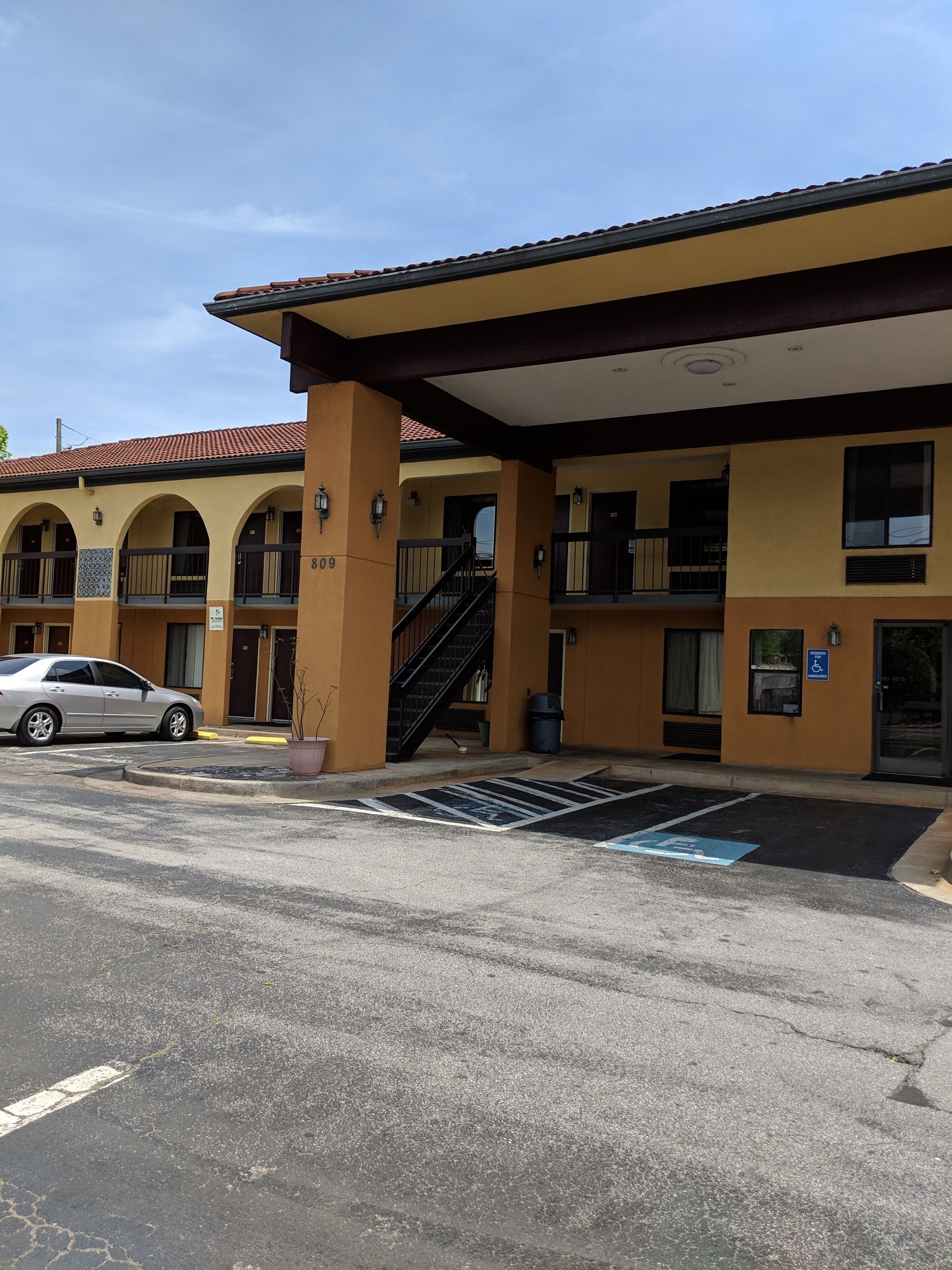 A two-story building with a yellow facade, a covered parking area, and a handicapped parking space.
