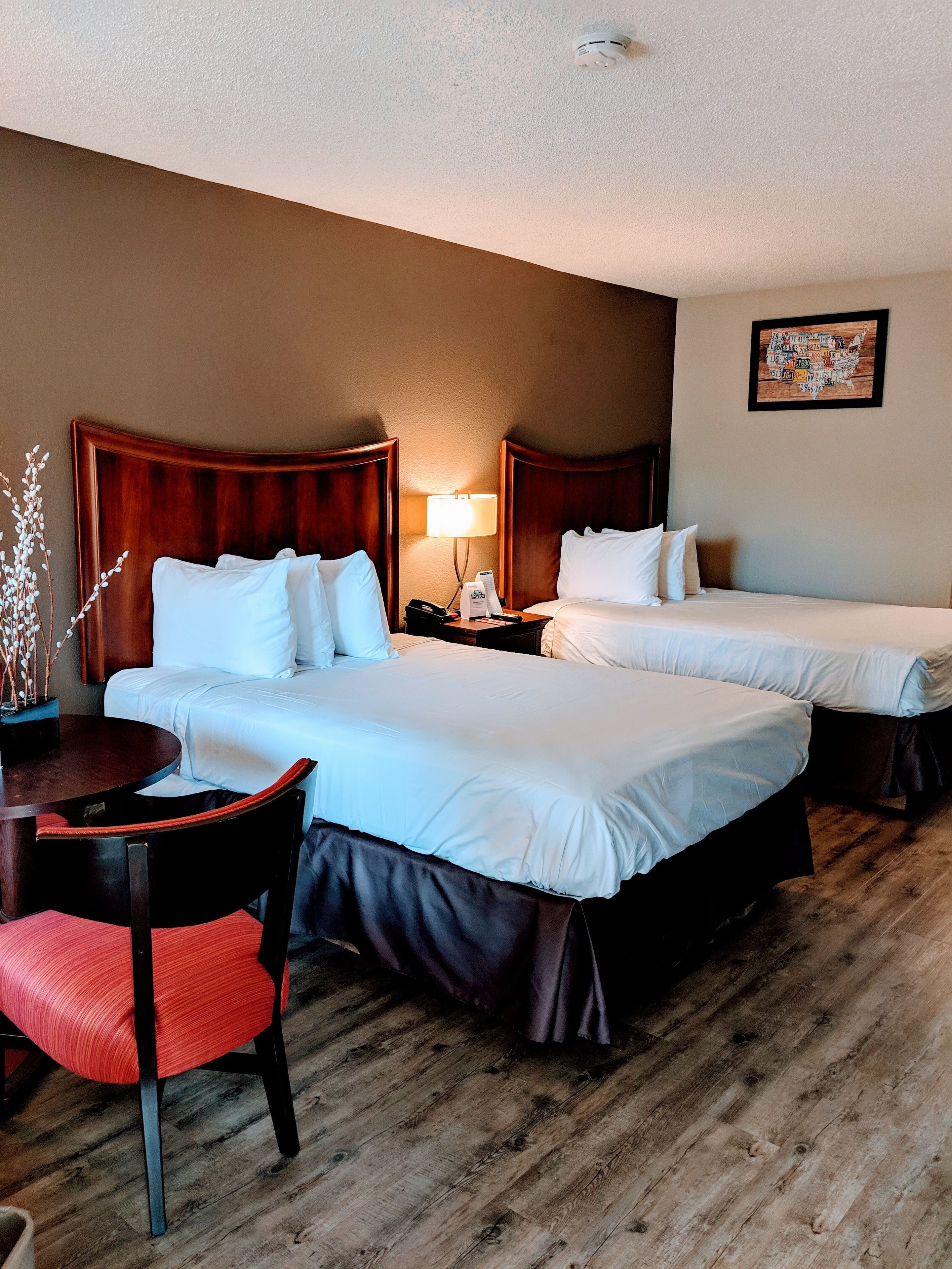 Une chambre d’hôtel avec deux lits, un bureau avec une chaise, une lampe et un tableau accroché au mur.