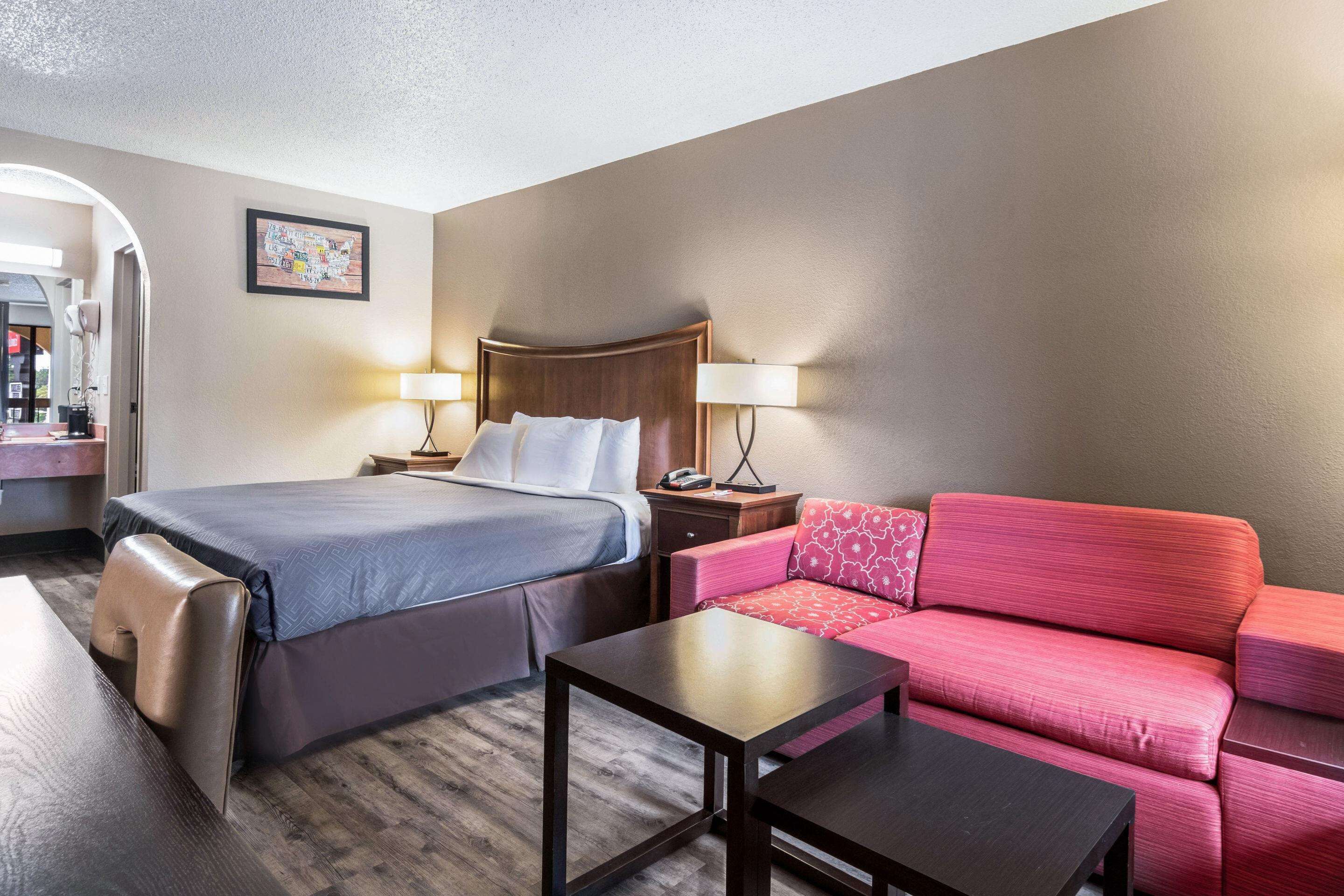 Una habitación de hotel con cama, sofá rojo, una mesita y una mesita de noche con lámpara.