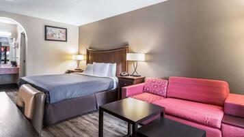 Una habitación de hotel con cama, sofá rojo, una mesita y una mesita de noche con lámpara.