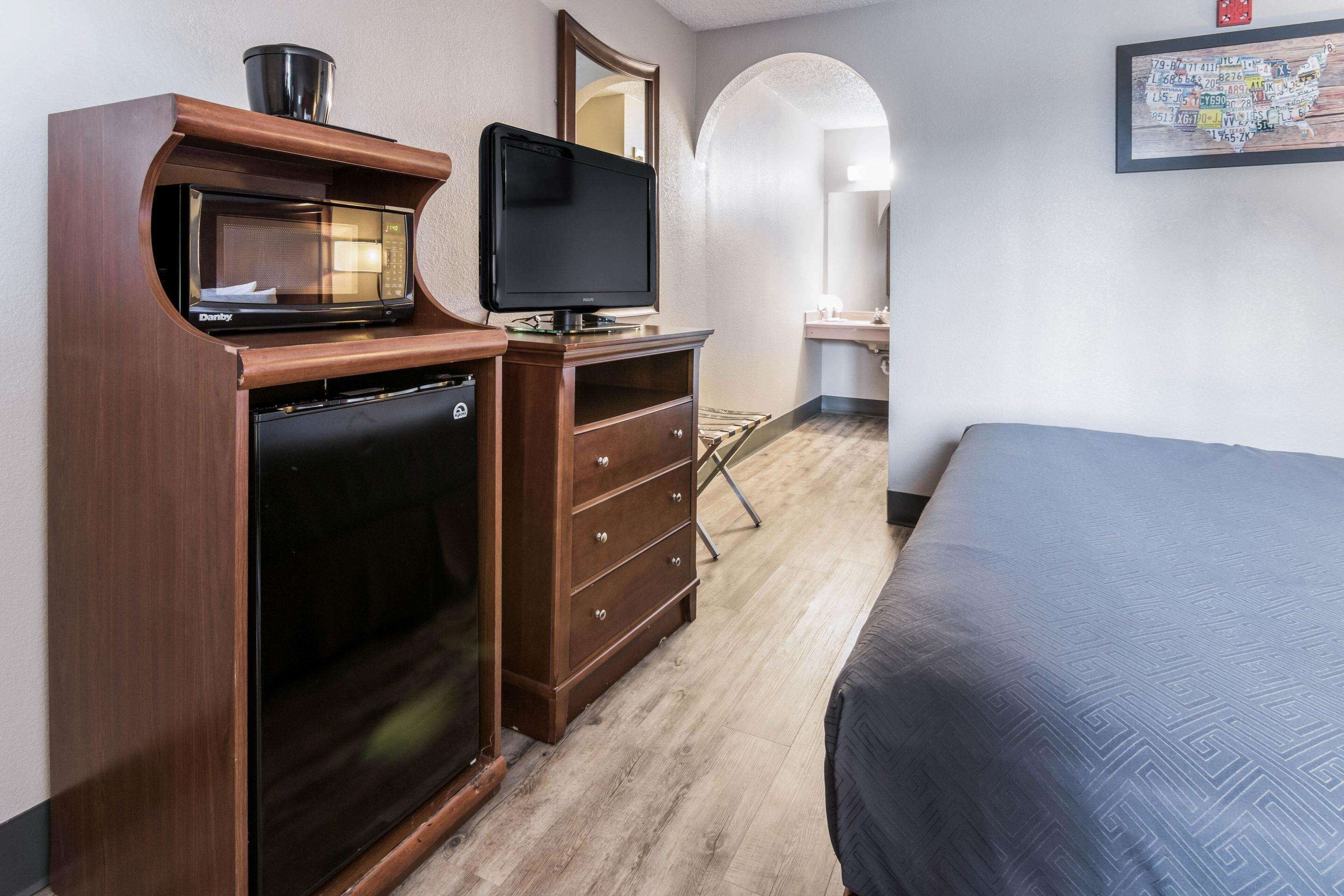 Habitación de hotel con un escritorio de madera, un televisor de pantalla plana, una cama y un baño visible a través de un arco.
