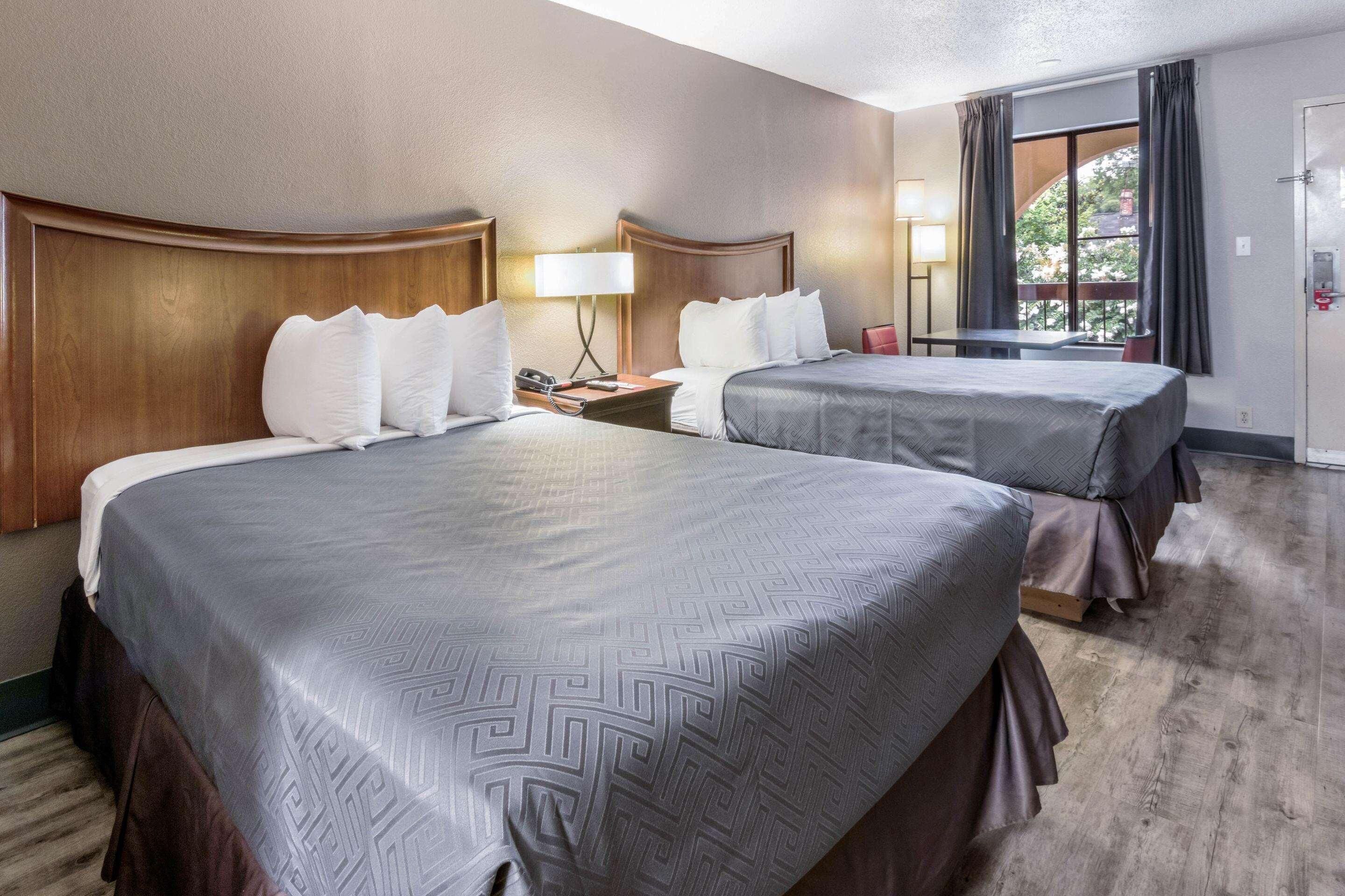 Habitación de hotel con dos camas, un escritorio, una silla, una ventana con cortinas y una puerta.