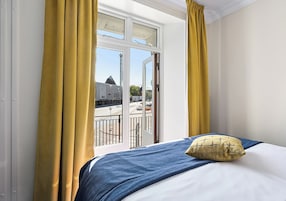 A hotel room with a bed, a view of a building outside, and yellow curtains.