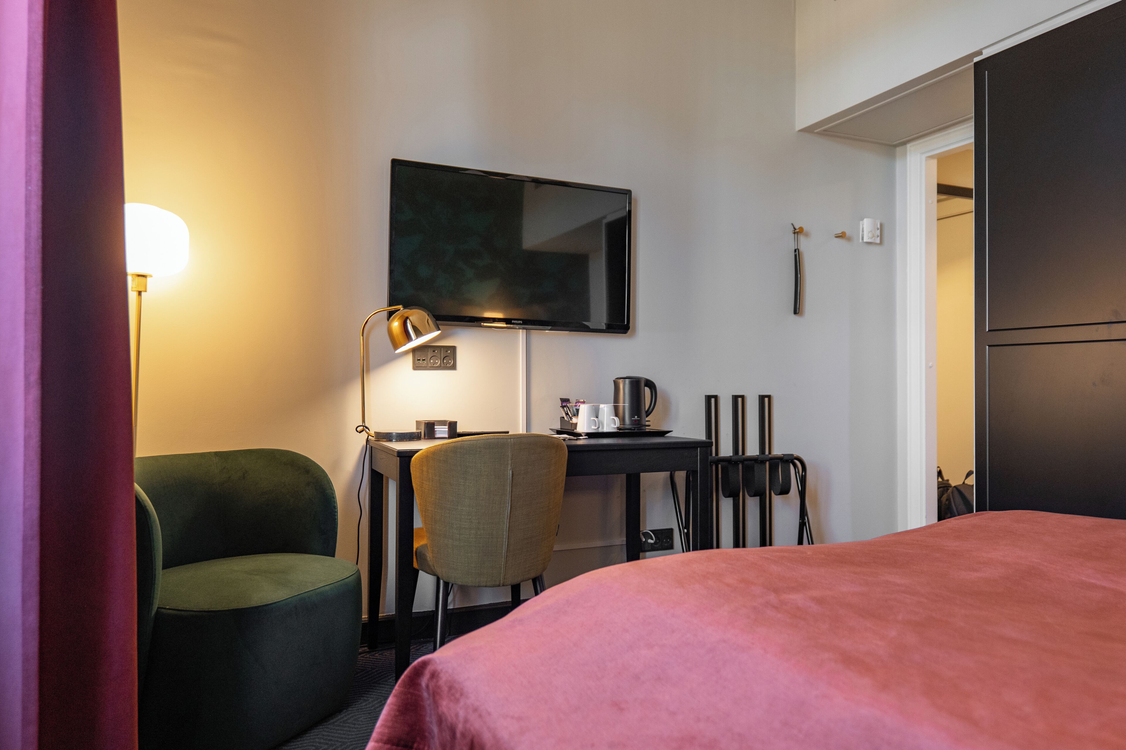 Une chambre d’hôtel avec un lit, un bureau, une chaise, une télévision et une porte.