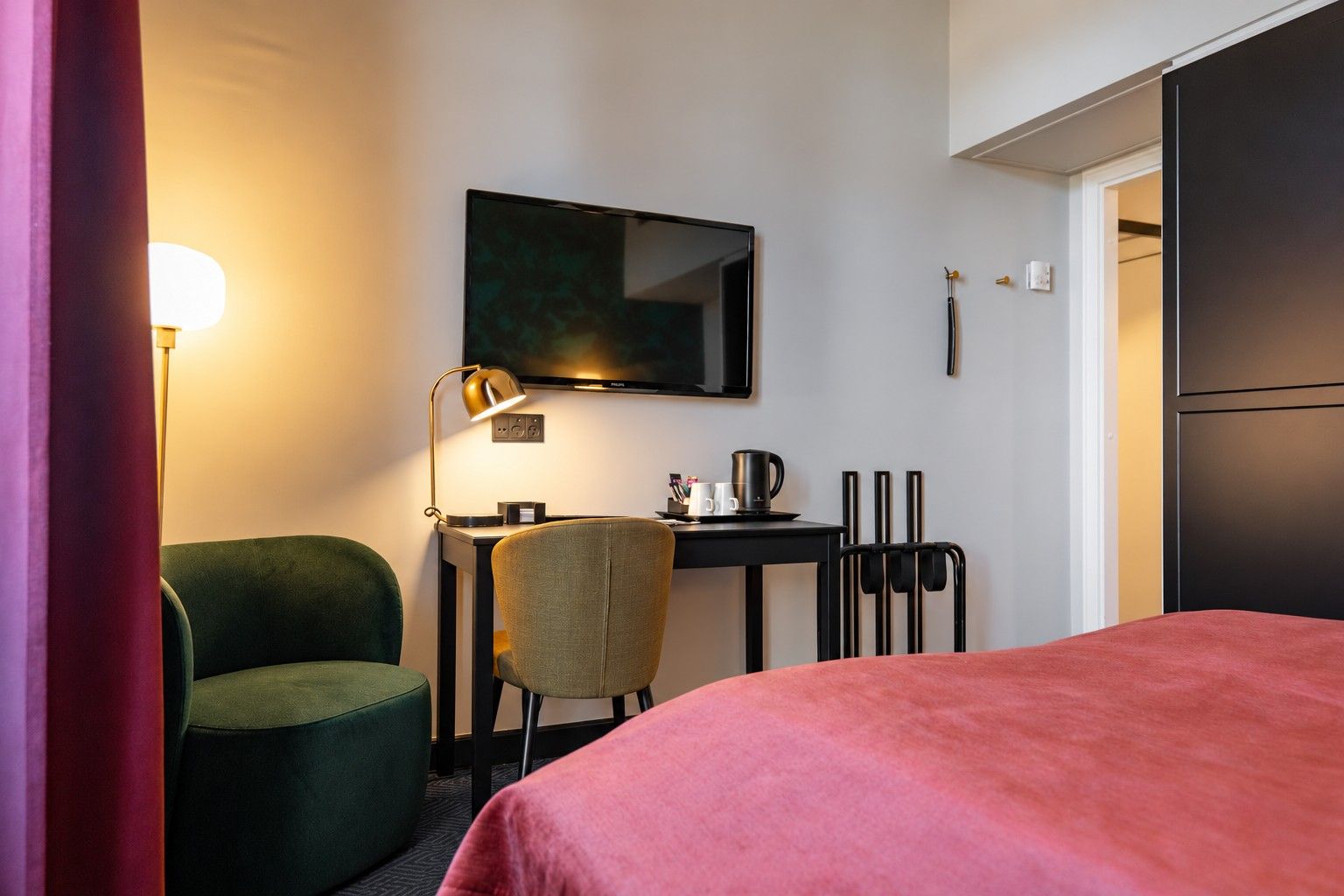 A hotel room with a bed, a desk with a chair, a television, and a lamp.
