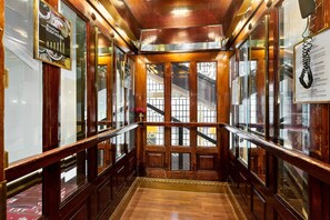 Interior d'un ascensor de fusta amb portes de vidre i una barana metàl·lica.