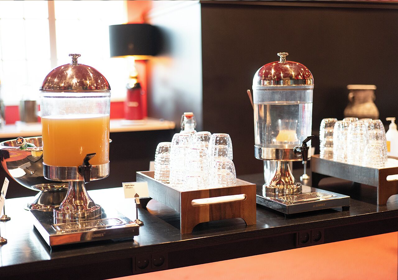 Una zona de bar con una máquina de café, un dispensador de zumo y una jarra de cristal.