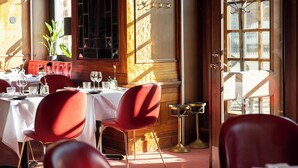 Interior de un restaurante con sillas rojas, mesas blancas y una planta en maceta.