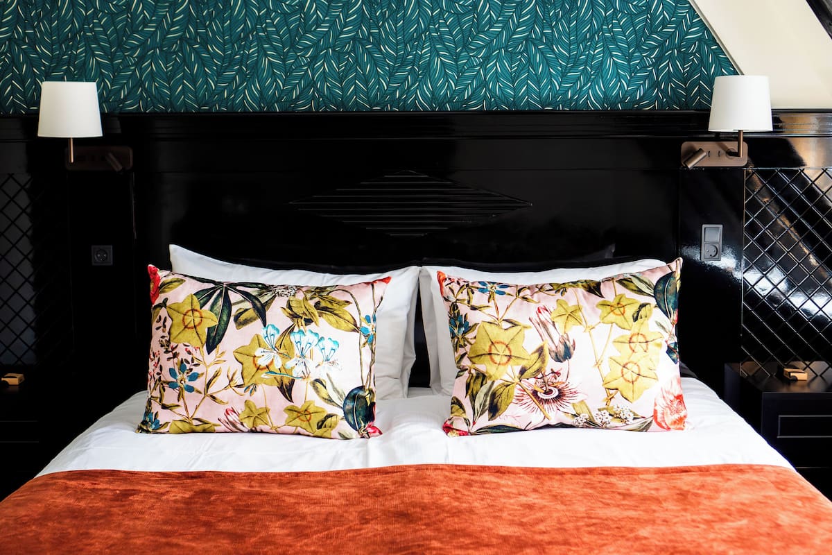 A bed with floral pillows, a black headboard, and a teal leaf-patterned wall.
