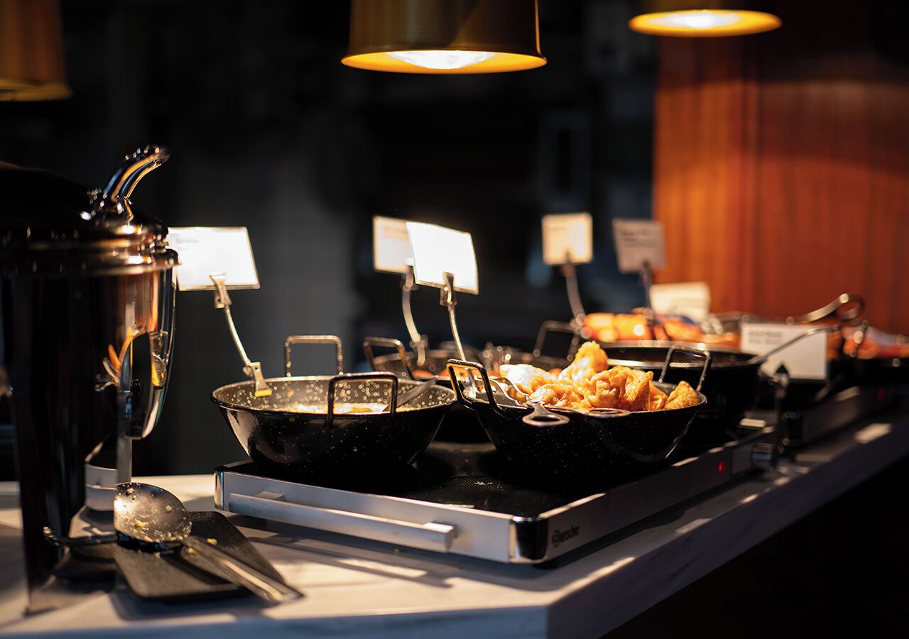 A buffet setup with various dishes in black serving containers, a spoon, and a sign indicating the type of food.