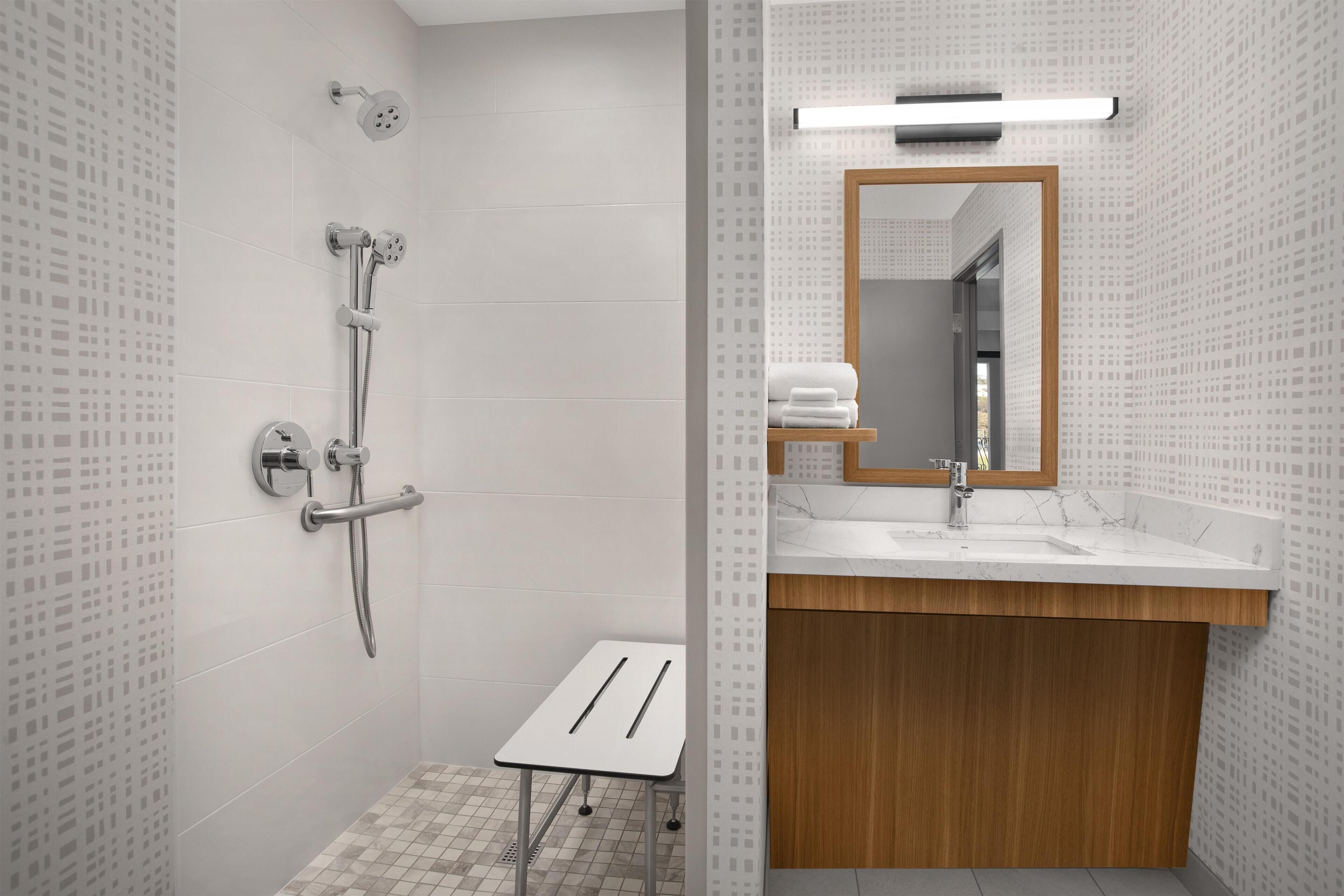 A modern bathroom with a shower, a small table, and a vanity with a mirror.