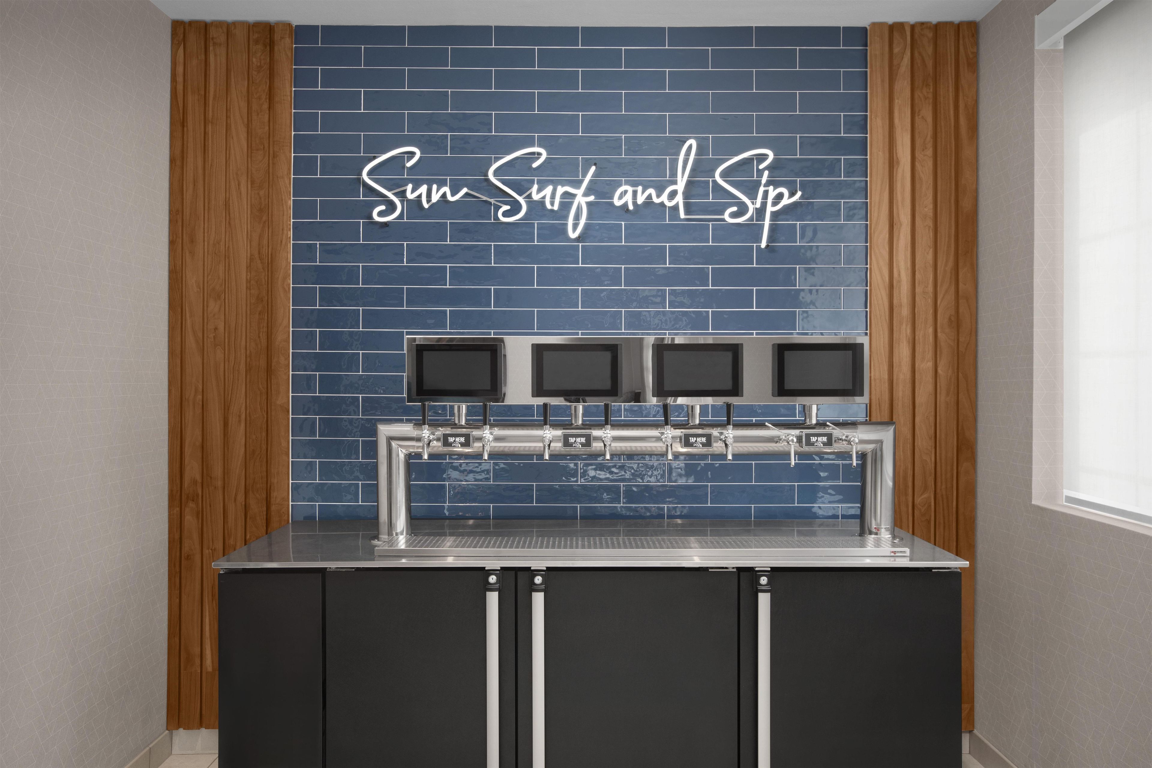 A bar area with a neon sign reading 'Sun Surf and Spa' above a row of taps.