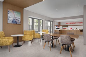 A modern dining area with yellow patterned chairs, a wooden table, and a breakfast bar with a sign.