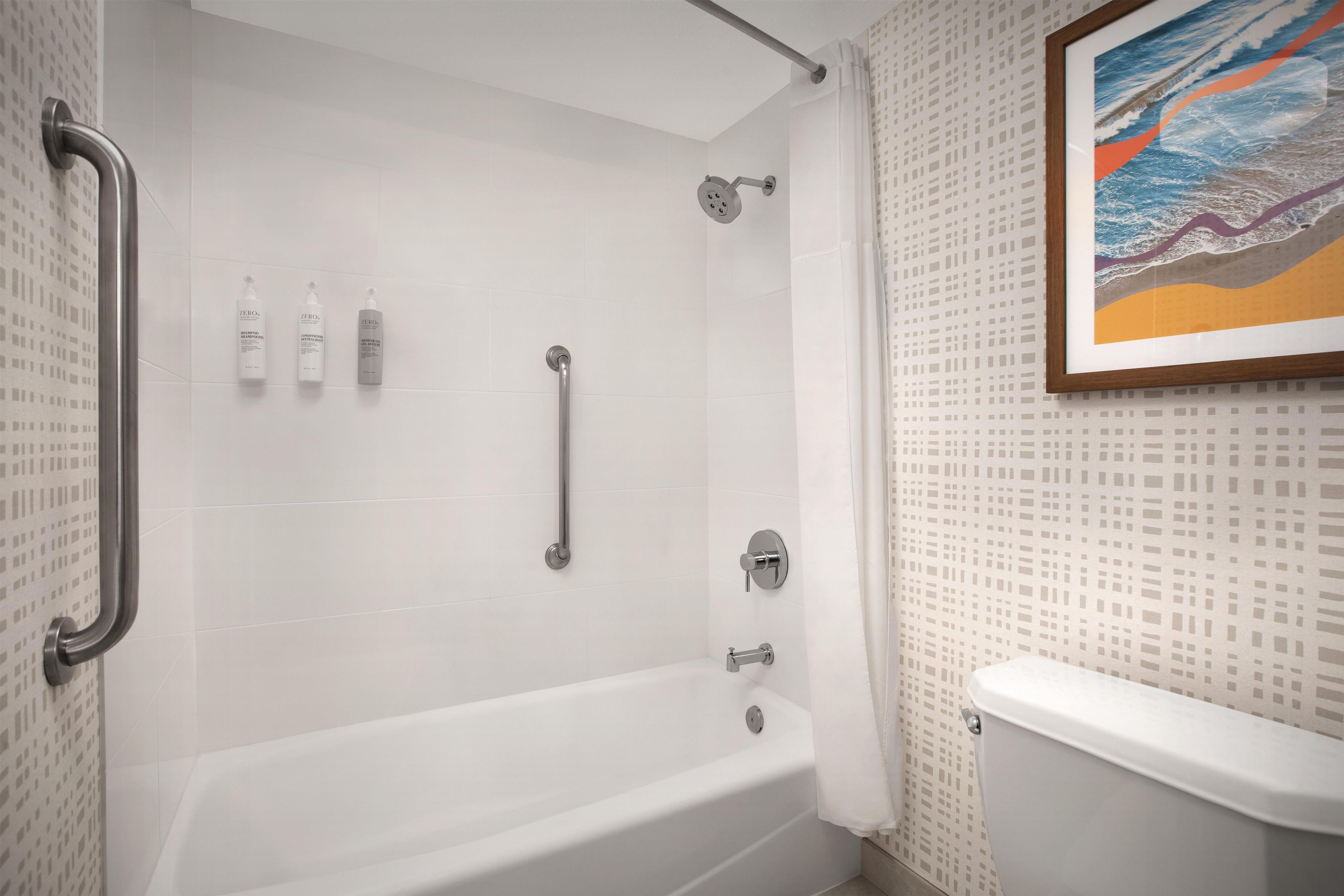 Un baño con bañera, ducha e inodoro. Hay tres botellas de champú y acondicionador en la pared.