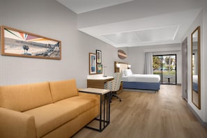 Quarto de hotel com sofá, escrivaninha, cama, cadeira e obras de arte nas paredes.