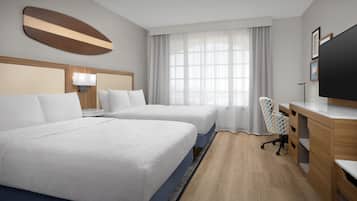 A hotel room with two beds, a desk, a chair, a TV, and a window with curtains.