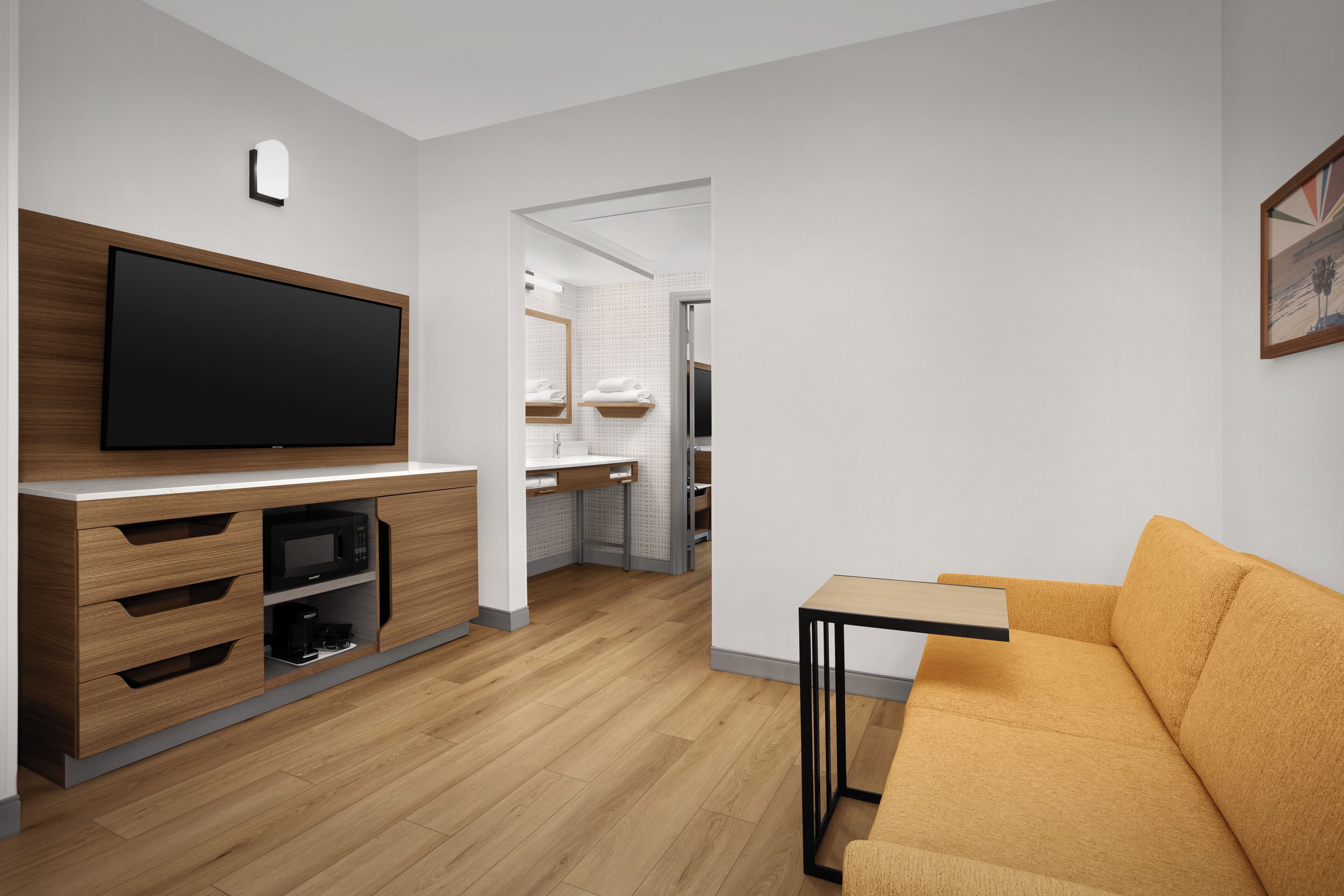 A modern living room with a flat-screen TV, wooden furniture, a sofa, and a kitchen area in the background.