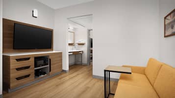 A modern living room with a flat-screen TV, wooden furniture, a sofa, and a kitchen area in the background.