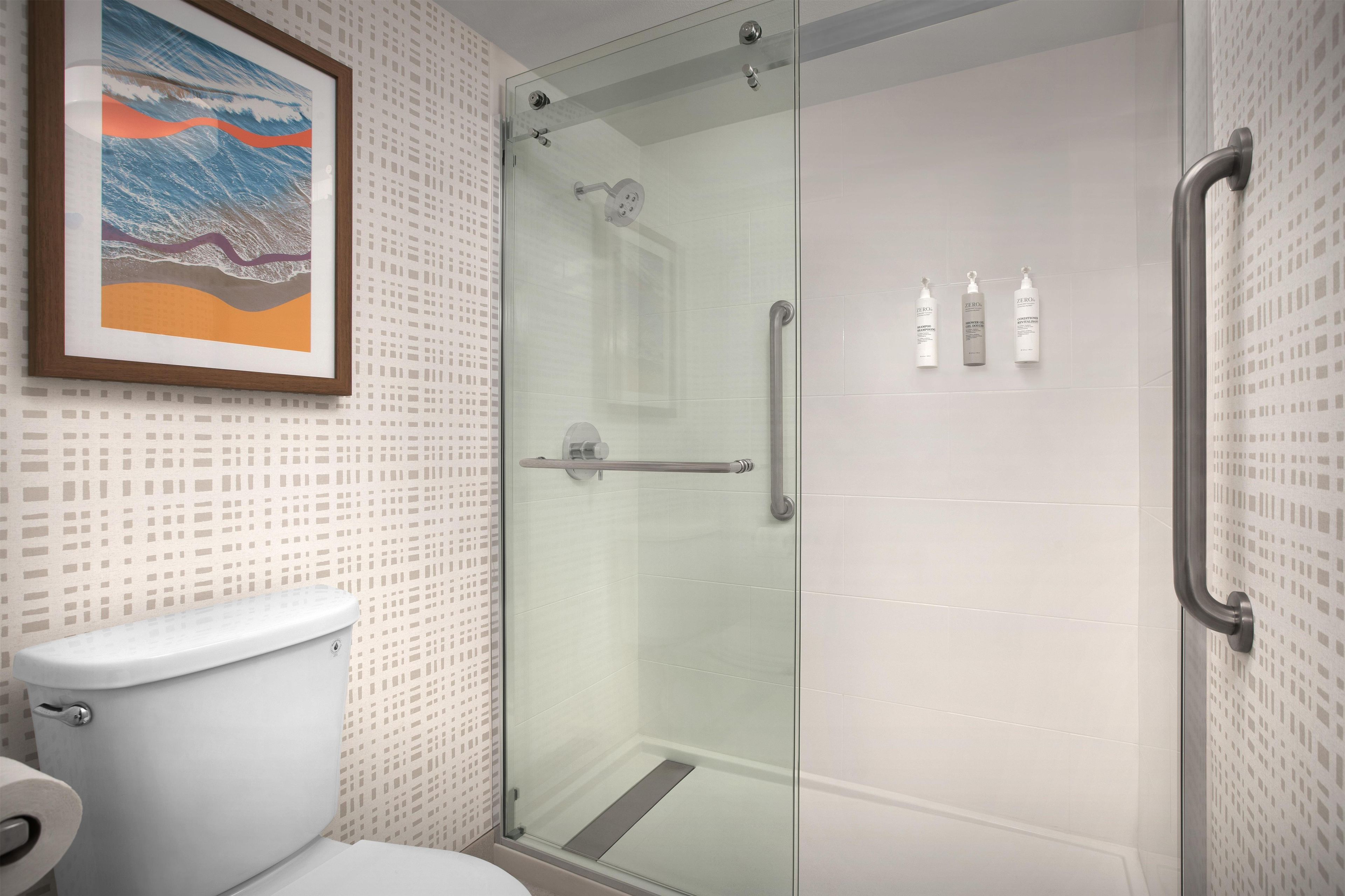 Un baño moderno con cabina de ducha de vidrio, inodoro y una obra de arte enmarcada en la pared.