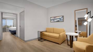 A modern hotel room with a sofa, armchair, small round table, and a painting on the wall.