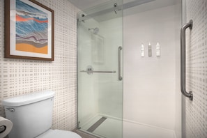 A modern bathroom with a glass shower enclosure, a toilet, and a framed artwork on the wall.