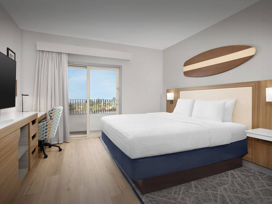 A hotel room with a bed, desk, chair, TV, and a balcony view.