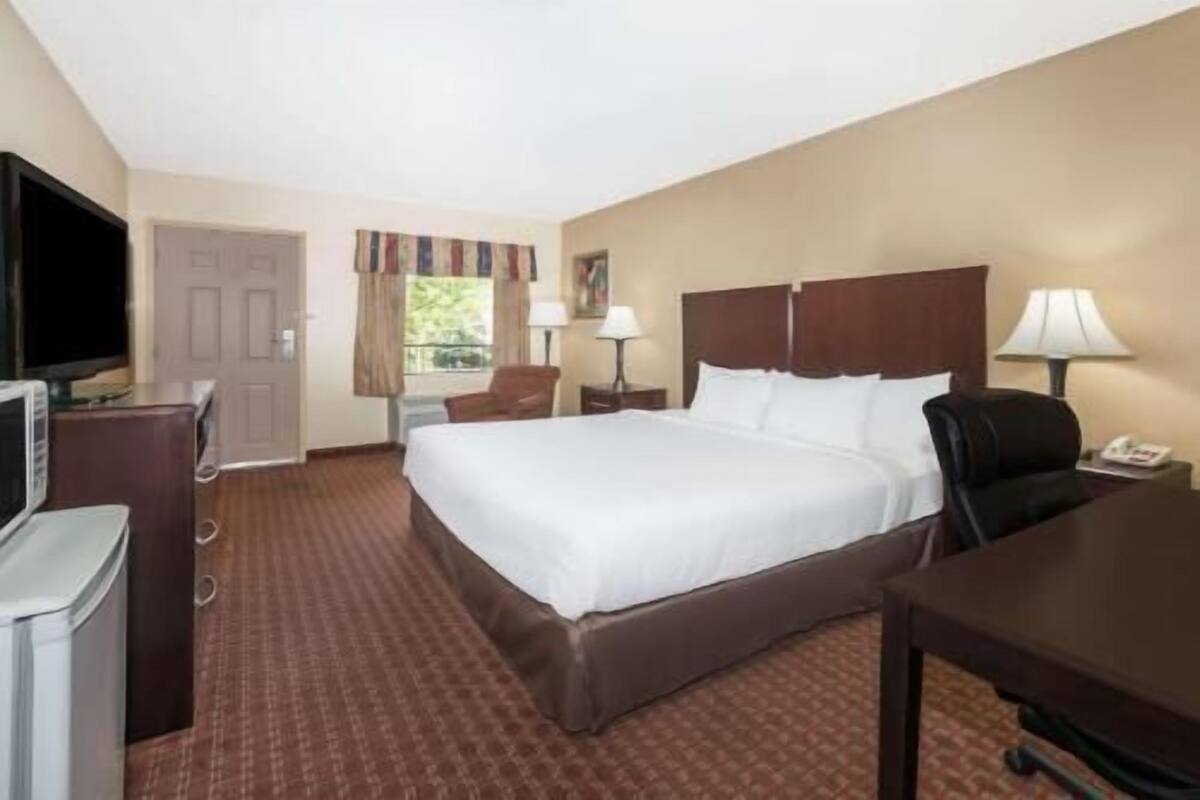 Habitación de hotel con cama, escritorio, silla, televisor y ventana con cortinas.