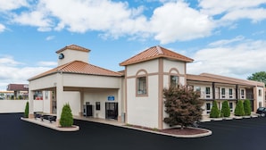 A hotel with a lobby, a parking lot, and a building with a brown roof.