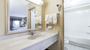 A hotel bathroom with a sink, mirror, towel rack, and a visible toilet.