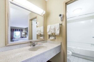 Un baño de hotel con lavamanos, espejo, toallero y un inodoro a la vista.