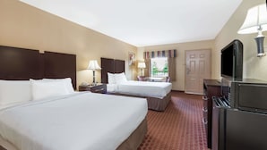 A hotel room with two beds, a TV, a desk with a chair, a window with curtains, and a door.